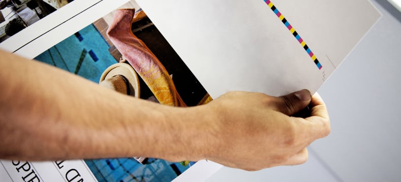 A hand holding a printed booklet cover showing trim marks